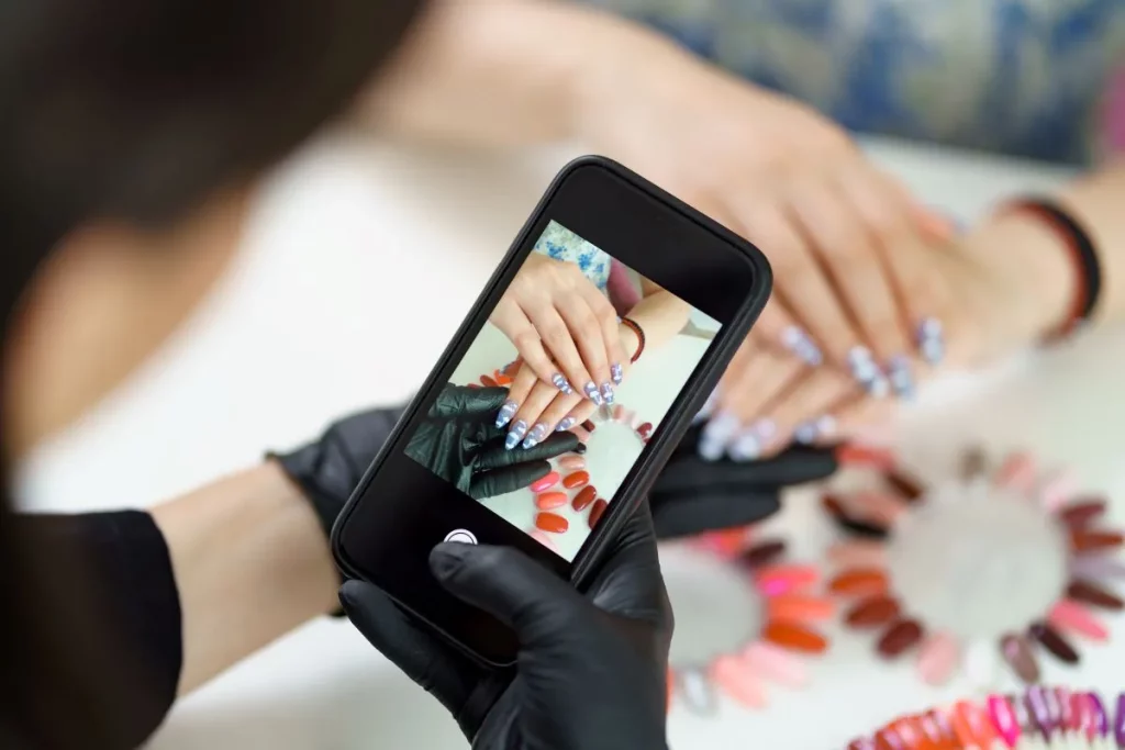 Manicurist wearing gloves taking a photo of client's manicured nails with a smartphone camera.