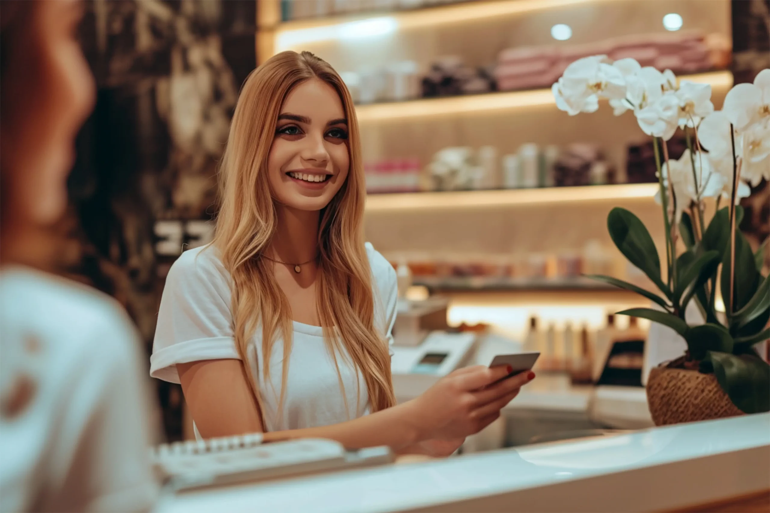 Female receptionist smiles while holding a credit card at beauty salon before using salon POS system.